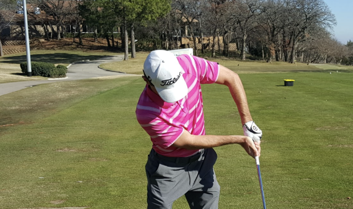 Golfer in pink Titleist shirt through impact on an Austin, Texas course showing a bent lead arm chicken wing position that causes loss of distance, weak strikes, and inconsistent ball flight in the golf swing