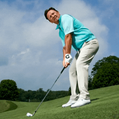 Golfer hitting shot with ball below feet on sloped lie